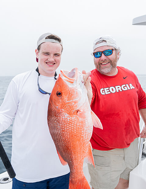 An older and younger man smiling and holding up the fish they caught.